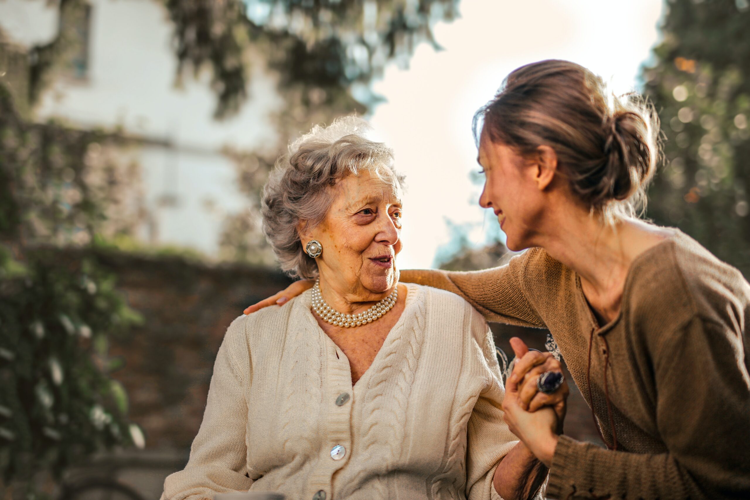 Elderly mother and her daughter sitting outdoors, deeply engaged in conversation as the mother shares her life stories, portraying a moment of intergenerational bonding.