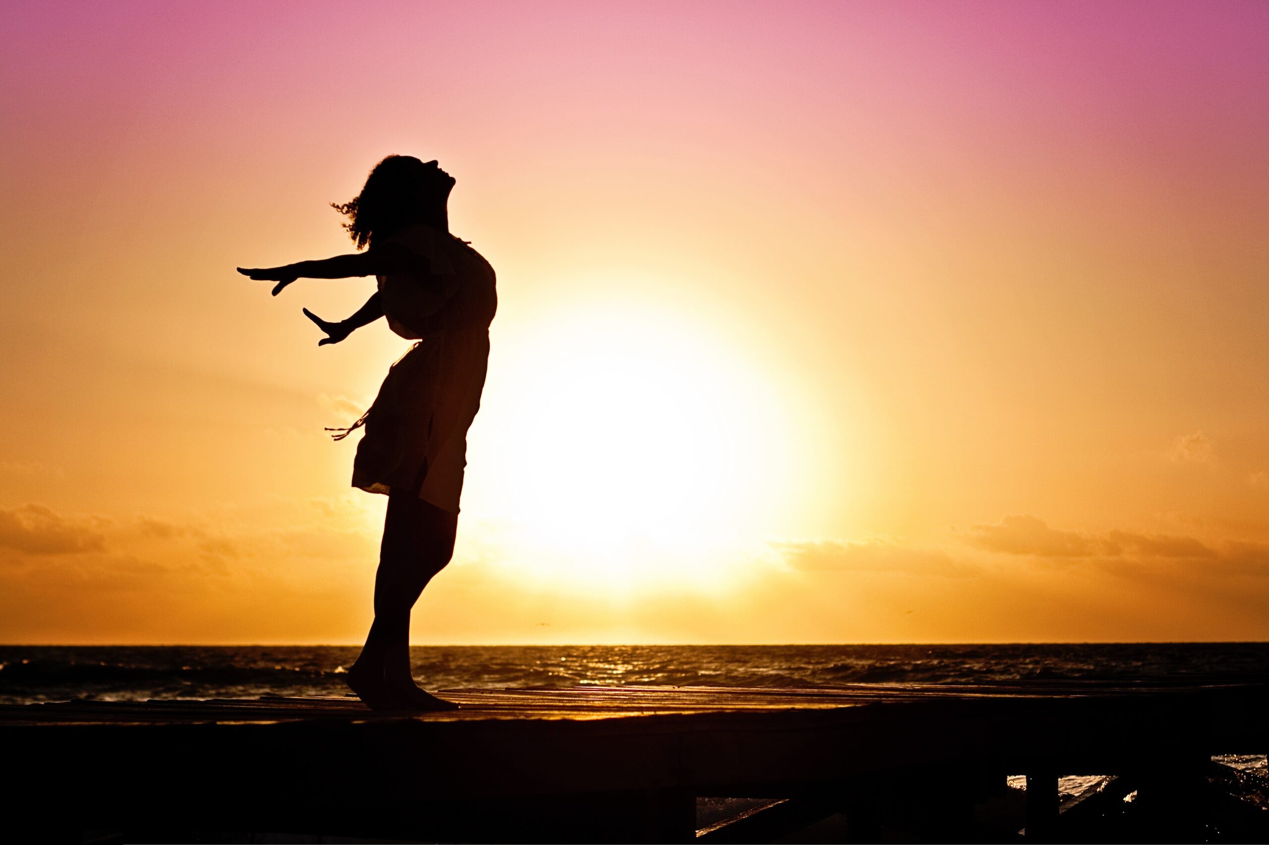 Confident woman silhouetted against a radiant sunset, symbolizing the empowerment and personal growth attained through sharing life experiences.